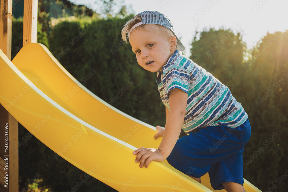 Happy little boy play outdoor on the children playground and ride the yellow plastic children's slide in the summer
Happy little boy play outdoor on the children playground and ride the yellow plastic children's slide in the summer