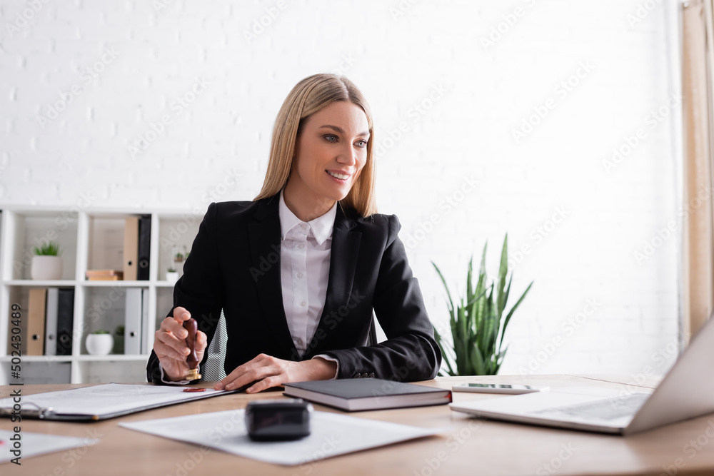 smiling notary looking at laptop while stamping contract in office. smiling notary looking at laptop while stamping contract in office.
