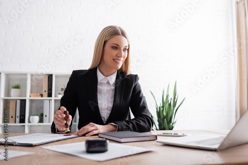 smiling notary looking at laptop while stamping contract in office. photo