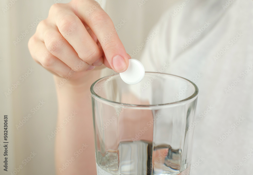 A woman's hand puts a soluble tablet in a glass of water A woman's hand puts a soluble tablet in a glass of water