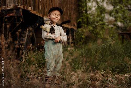 Beautiful toddler boy, child in vintage clothing, playing with little chicks in the park under blooming tree in garden