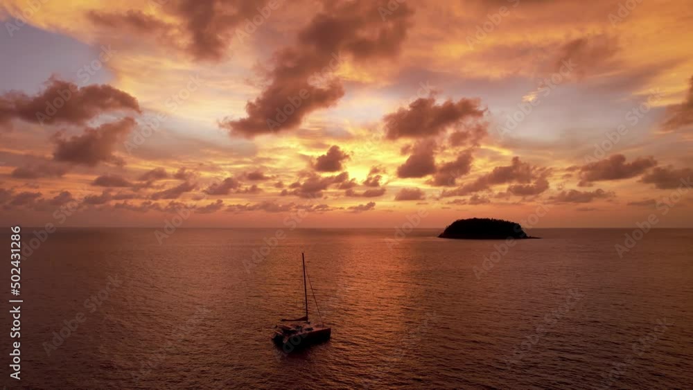 Luxury yacht at an epic sunset with a view of the island and incredible orange clouds. The sky is reflected in the water. A lonely island in the distance. Calm. Top view from drone. Kata Beach Phuket Luxury yacht at an epic sunset with a view of the island and incredible orange clouds. The sky is reflected in the water. A lonely island in the distance. Calm. Top view from drone. Kata Beach Phuket