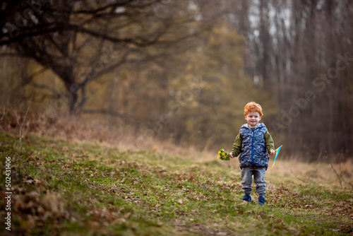 A little boy runs in the park with the flag of Ukraine and holds a bouquet of spring flowers © Iryna Savchuk