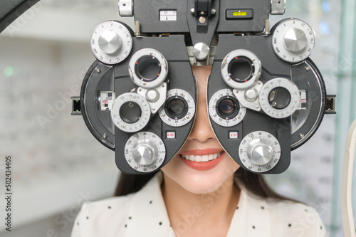 Young female customer being examined visual test using Bifocal Optometry eyesight measurement device by ophthalmologist in optical center, eyecare concept.