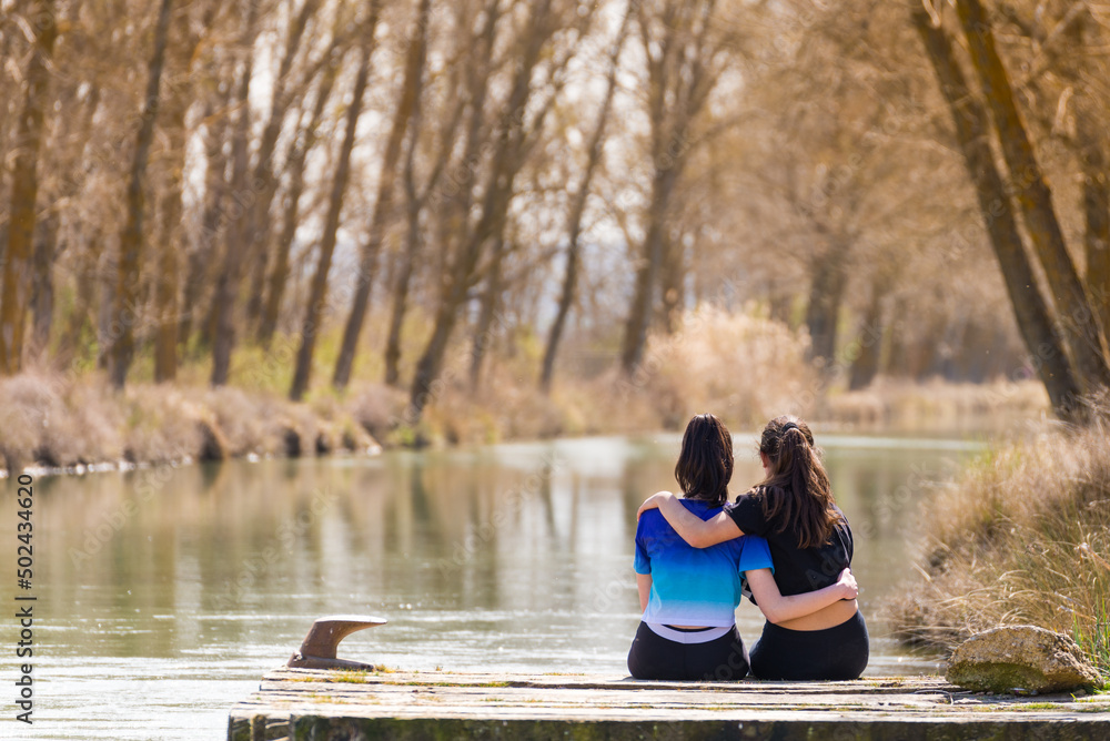 Two teenage girls sitting on a pier look out over the canal