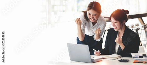 Two Elegant businesswoman sitting in office with laptop. Excited asian business people raising hands to congratulate while working on laptop in office.