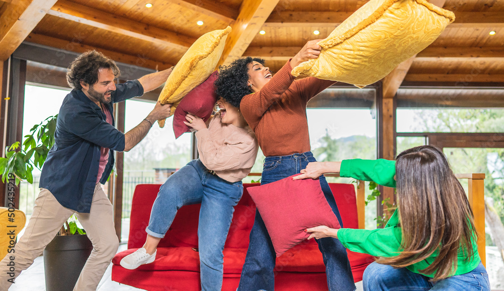 Happy multicultural friends having fun pillow fight in living room
