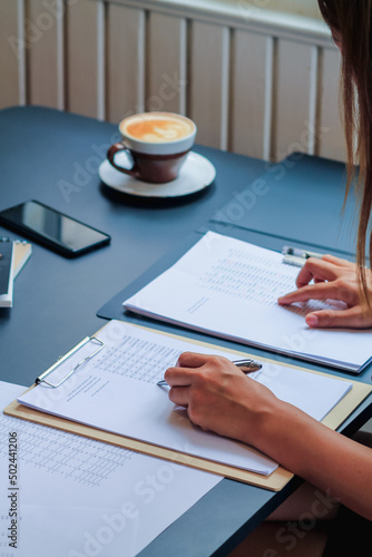 Fotografie An accountant is examining a large amount of income and expense documents laying on their desks in their offices to summarize their annual results