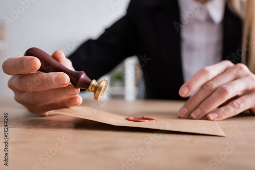 selective focus of stamper and sealed craft paper envelope in hands of cropped notary on blurred background. photo