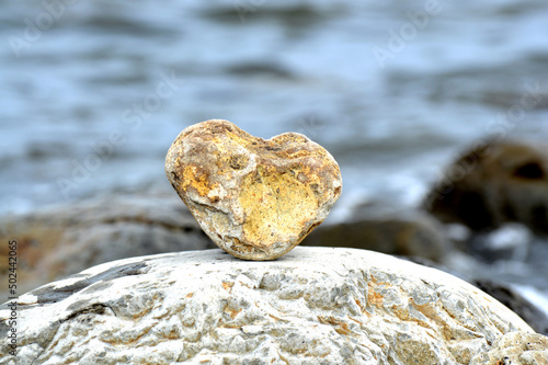 Heart shape stone against background of beach. Summer sunny day. Love, wedding and Valentine day concept. Finding beautiful and interesting stones. Beach vacation. 