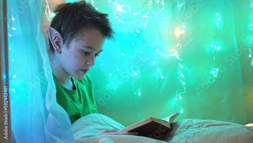 a teenager with long ears reads a book sitting on a bed decorated with garlands. wrapped in a blanket. elf costume