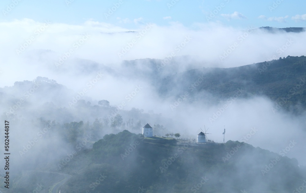 Molinos de viento tradicionales envueltos en niebla. Molinos de viento en lo alto de una colina envueltos por la bruma de la mañana en Sanlúcar de Guadiana, Huelva, España.