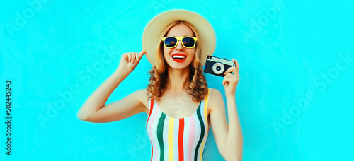 Summer portrait of happy smiling young woman photographer with film camera wearing straw hat on blue background, blank copy space for advertising text