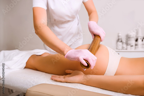 The masseur makes a bamboo massage to a young woman.