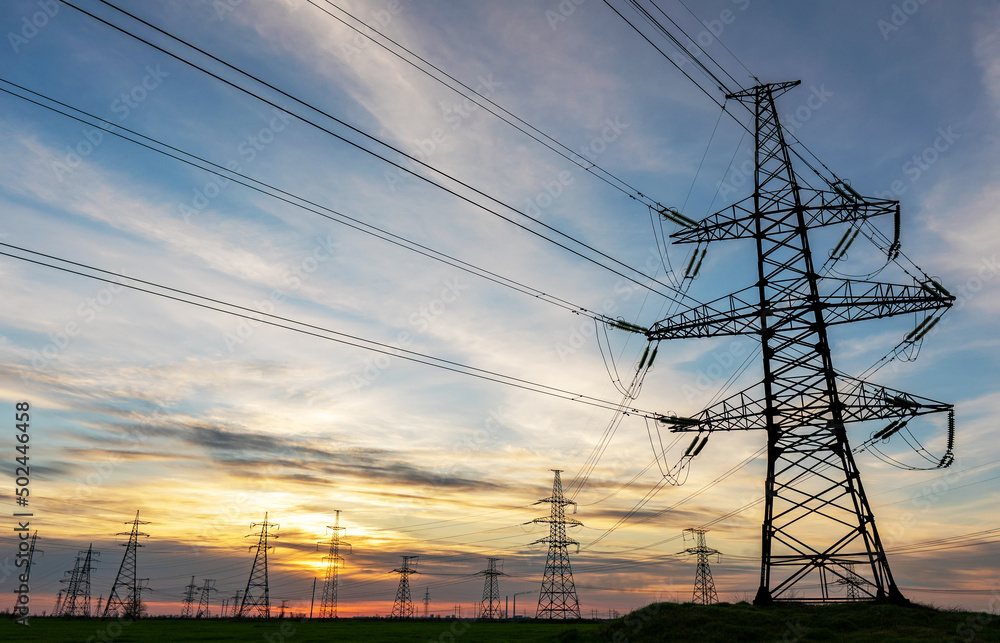 high voltage power lines in the field against the backdrop of a bright and colorful sunset or dawn