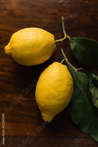Close up of two large yellow lemons with branch and leaf on a wooden background 
