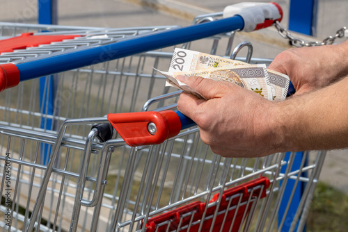 Shopping cart in a supermarket and Polish zloty money, held in hand, Concept of inflation, Rising costs of living, Home budget in Poland photo