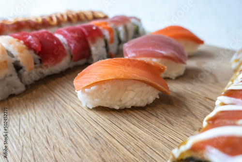 Angled, selective focus view of a variety of sushi rolls on a bamboo cutting board