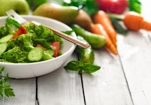 Healthy food concept. Bowl with fresh summer salad and ingredients on white wooden table copy space