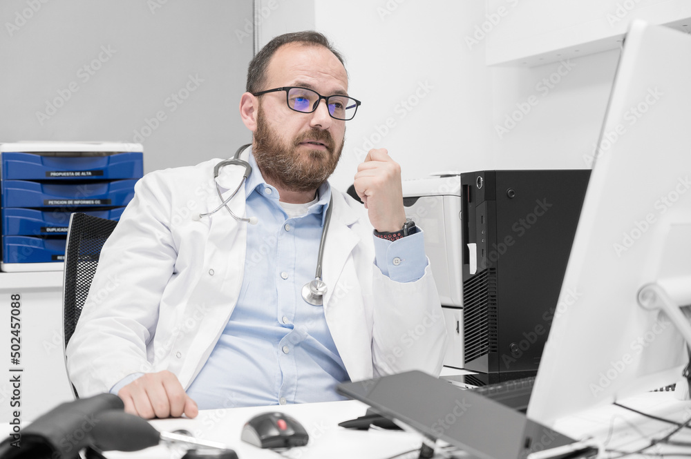 Portrait of friendly smiling healthcare professional therapist sitting at workplace. Happy confident male doctor physician wearing white medical coat and stethoscope. High quality photo Portrait of friendly smiling healthcare professional therapist sitting at workplace. Happy confident male doctor physician wearing white medical coat and stethoscope. High quality photo
