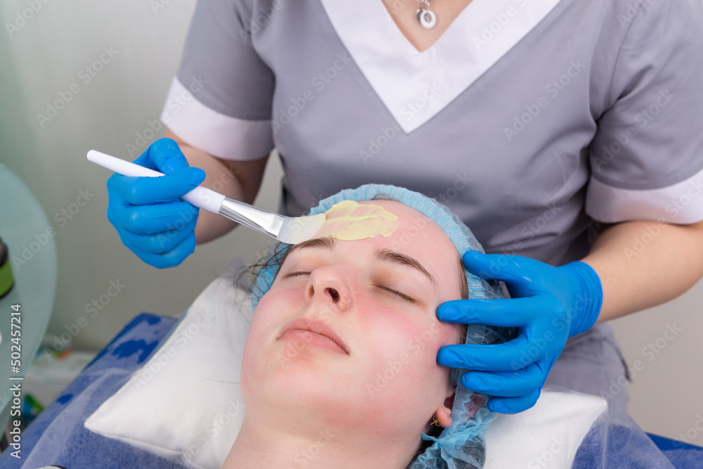 Cosmetologist applies alginate mask with spatula on face of woman. Cosmetologist applies alginate mask with spatula on face of woman.