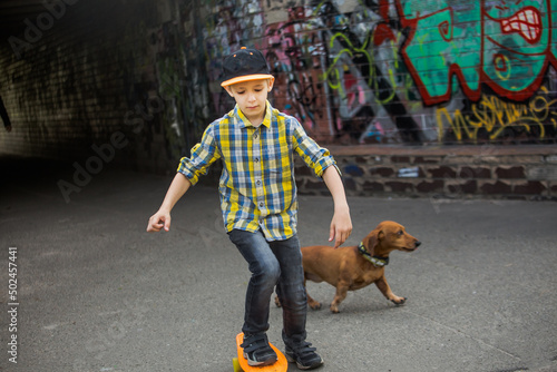 A boy walks in town with a dog. Active games of children. A child rides a skateboard on the road in the spring.