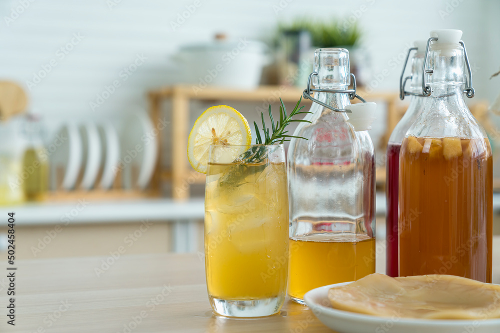 Kombucha tea with lemon and sweetened root filling in glass jug on kitchen background. Natural kombucha fermented tea beverage healthy organic drink in glass. Kombucha tea with lemon and sweetened root filling in glass jug on kitchen background. Natural kombucha fermented tea beverage healthy organic drink in glass.