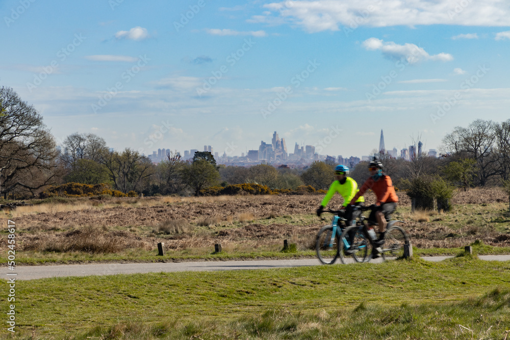 Cyclists in Richmond Park pass a stunning backdrop of the buildings in the centre of London Cyclists in Richmond Park pass a stunning backdrop of the buildings in the centre of London