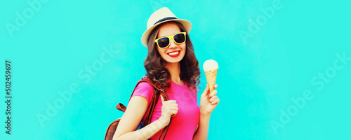 Portrait of happy smiling young woman with ice cream wearing summer straw hat on blue background