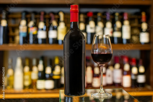 Bottle and glass of red wine in a store with a variety of bottles in the background out of focus