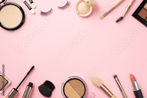 Top view photo of eyeshadow palette lipstick compact powder blush false eyelashes makeup brushes mascara on pastel pink background with copyspace