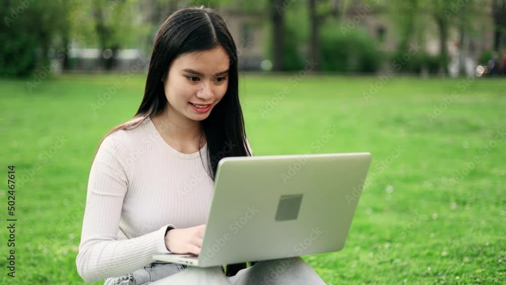 Attractive woman working at the laptop as sitting on grass in city park. Freelancer working in the park. Student at the campus. Attractive woman working at the laptop as sitting on grass in city park. Freelancer working in the park. Student at the campus.