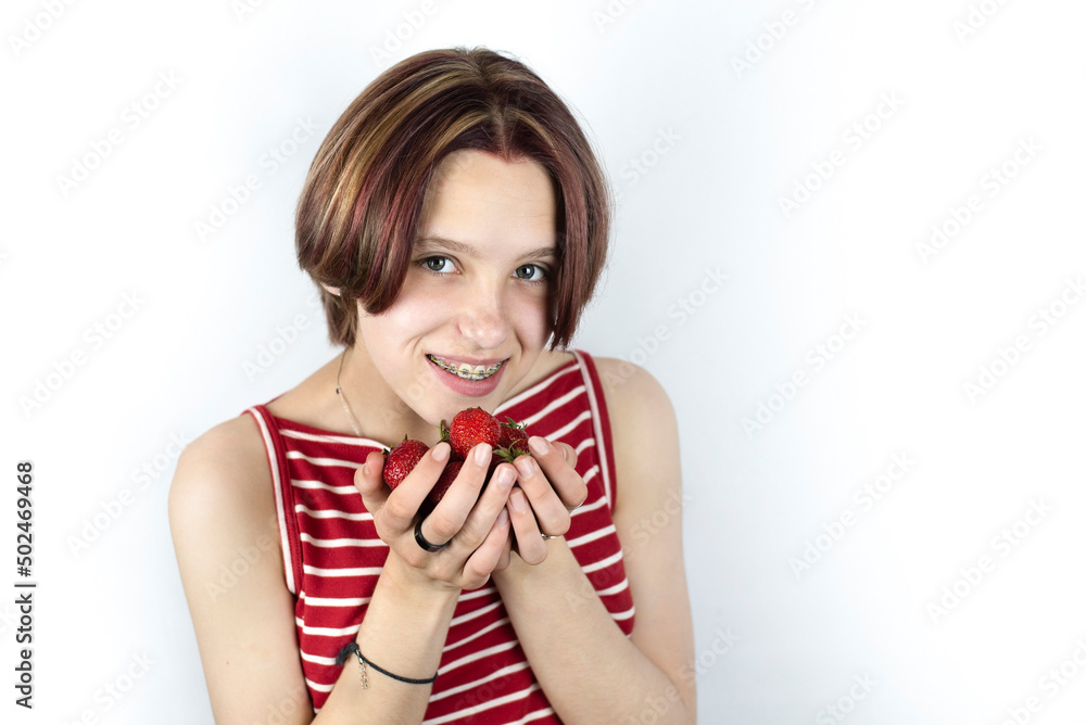 Teen girl with metal braces on her teeth smiles and holds a strawberry in front of her, the girl can not eat solid food so as not to break the braces. Dental concept Teen girl with metal braces on her teeth smiles and holds a strawberry in front of her, the girl can not eat solid food so as not to break the braces. Dental concept