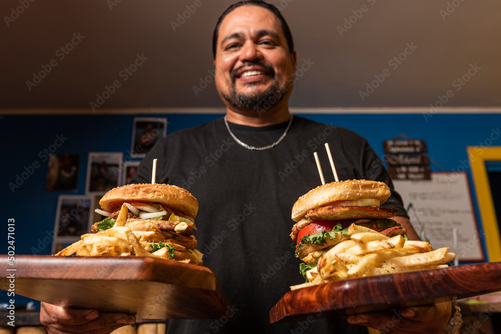 Latino male showing two large hamburgers with fries