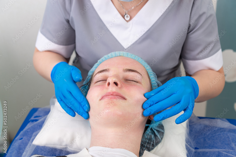 Naklejka premium A female cosmetologist manually treats the patient's skin with a moisturizing and toning gel.