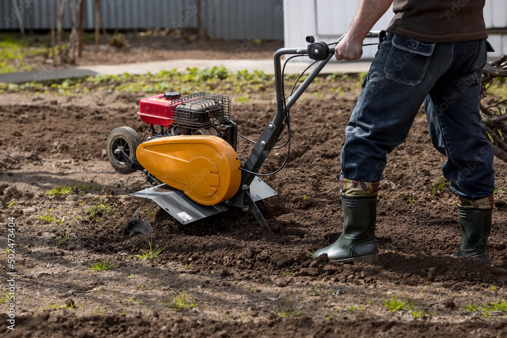 Obraz premium Banner. A male farmer plows the land with a cultivator. Agricultural machinery for tillage in the garden, combine harvester.
