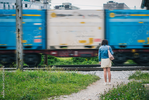 Woman waiting for the train to dissappear on an illegal crossingin a city. Dangerous crossing with a train. photo