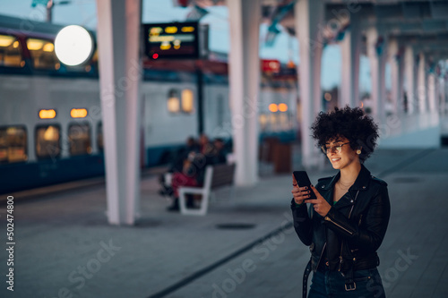 Woman waiting on a train station platform and using smartphone