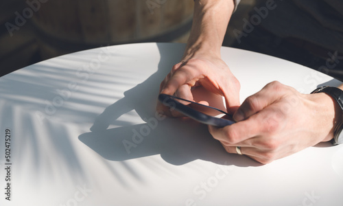 Close-up of mobile phone in hands on white table. Sunlight.