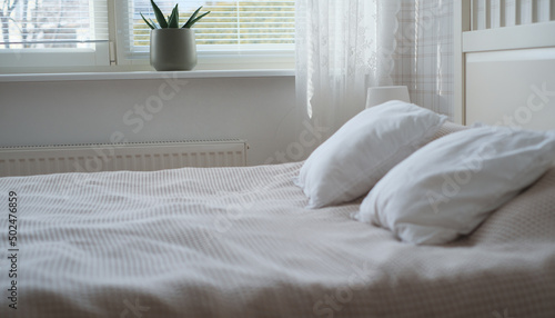 The interior of the room in white tones with a bed, bedside table, table lamp and a flower on the windowsill photo