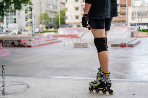 unrecognizable young man in an urban skateboard park with rollers on, wearing protective gear