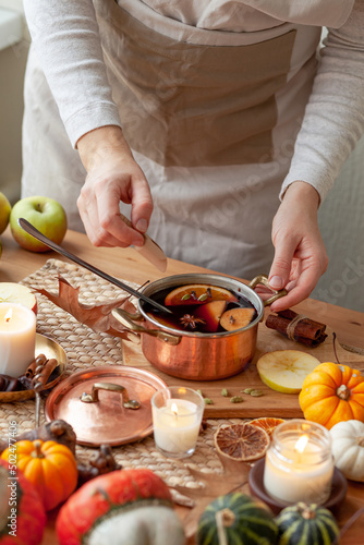 Young woman preparing hot autumn drink: mulled wine with spices, fruits. Natural ingreduents: cinnamon, anise, cardamon, clove, apple, orange. Cozy home atmosphere