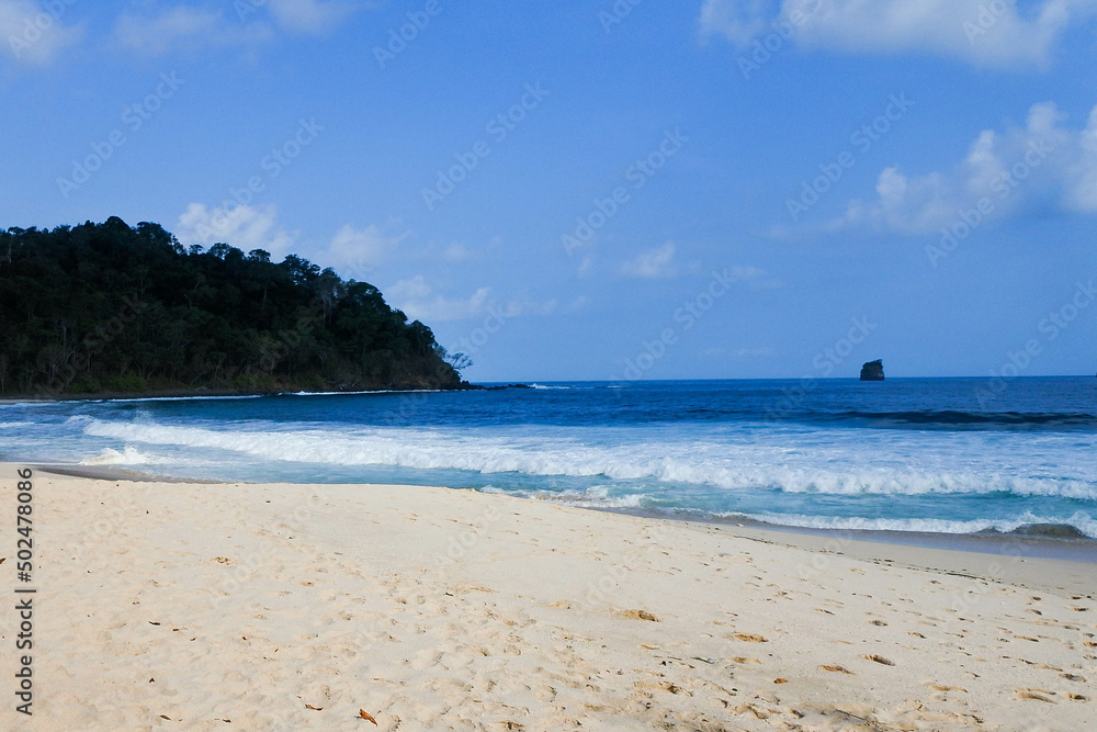 quiet white sandy tropical beach, with green islands on the horizon and gentle waves lapping
