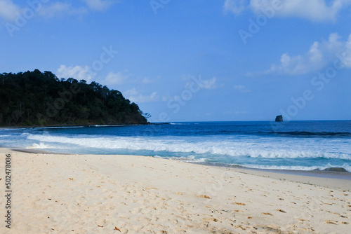 quiet white sandy tropical beach, with green islands on the horizon and gentle waves lapping