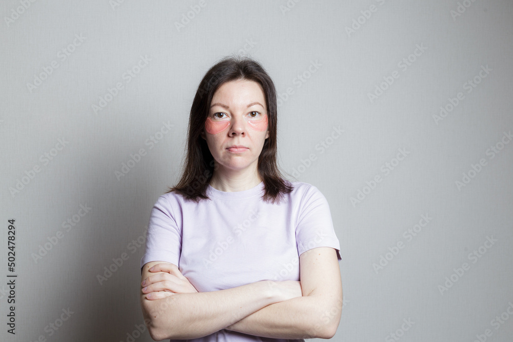 Fototapeta premium beautiful girl makes a cosmetic procedure. The girl uses eye patches. the woman crossed her arms over her chest. Pose of distrust