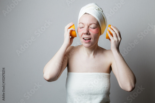 beautiful woman uses eye patches. The woman smiles and holds two halves of an orange as headphones. A woman listens to music. Rest after bath