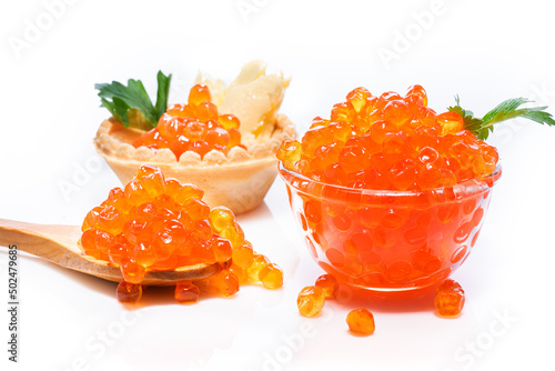 Red caviar on wooden spoon, next to it is glass plate with caviar and tartlet with red caviar close-up on white isolated background.