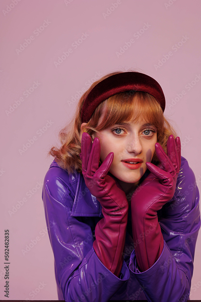 Young pretty girl in fashionable retro-style clothes, violet headband amd raincoat and gloves. Violet background. Beautiful lighting, unusual portrait Young pretty girl in fashionable retro-style clothes, violet headband amd raincoat and gloves. Violet background. Beautiful lighting, unusual portrait