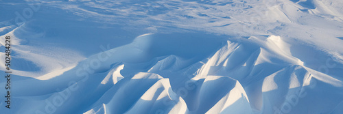 Snow texture. Wind sculpted patterns on snow surface. Wind in the tundra and in the mountains on the surface of the snow sculpts patterns and ridges. Arctic, Polar region. Winter panoramic background. photo