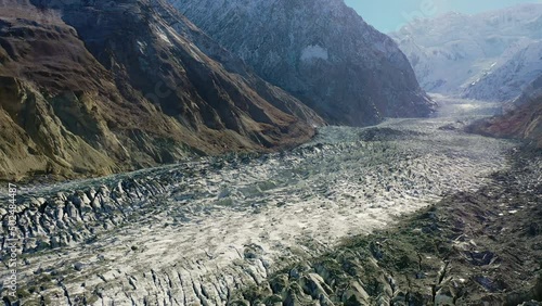 Aerial Moving Forward Over A Wide Glacier Surrounded By Steep Snowcapped Mountains - Hunza Valley, Pakistan photo